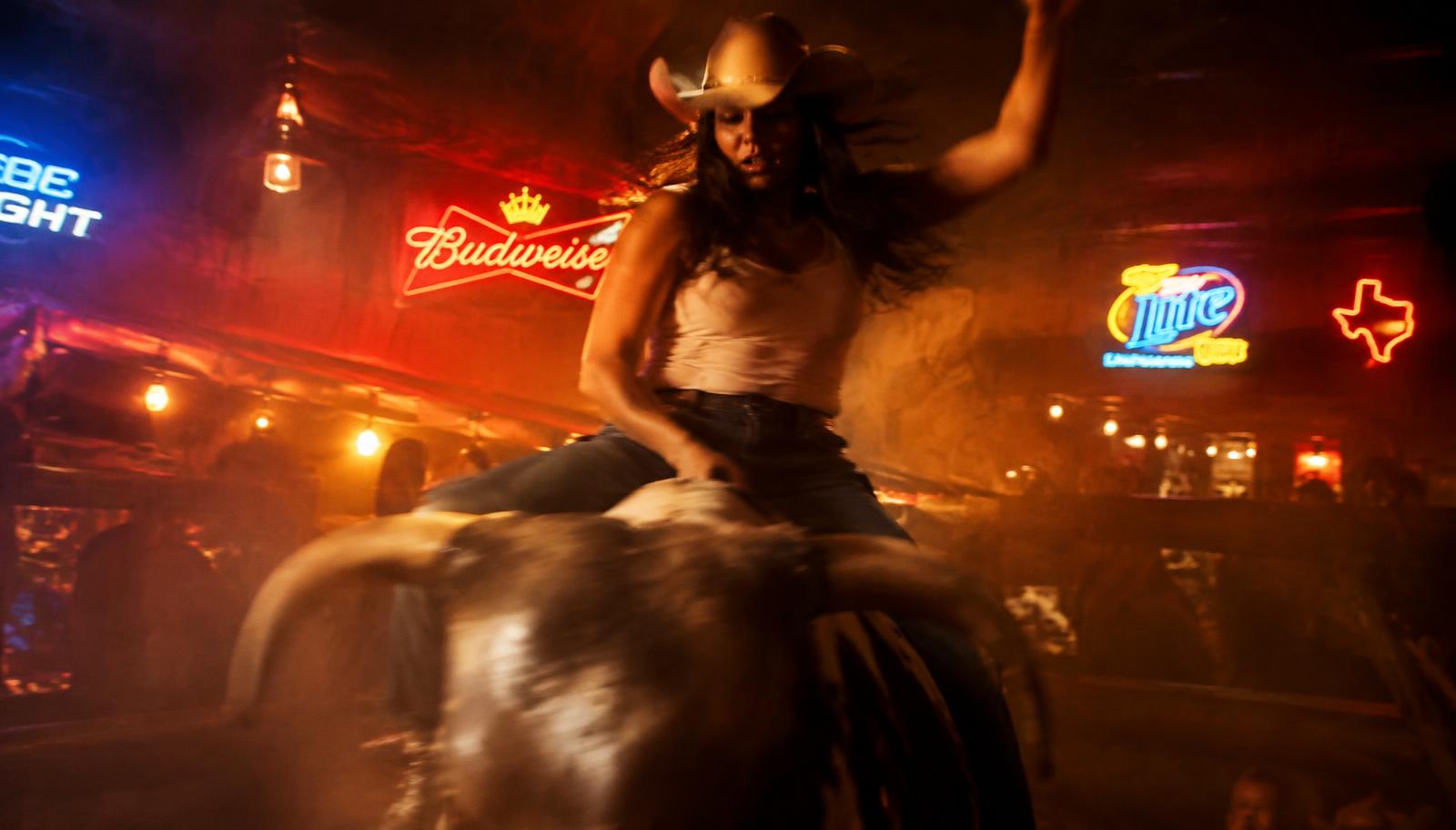 Woman riding a mechanical bull in a neon-lit bar